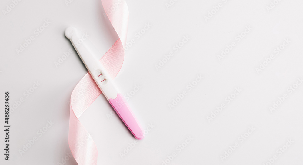 Pregnancy test kit. Positive woman pregnant test with pink silk ribbon on white background. New life and new family. Motherhood, pregnancy, birth control concept. Pregnancy test kit. Positive woman pregnant test with pink silk ribbon on white background. New life and new family. Motherhood, pregnancy, birth control concept.