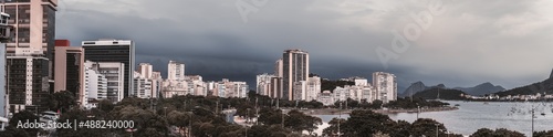 A panoramic view of Botafogo district of Rio de Janeiro, Brazil: an overcast day, many residential and office buildings, bay with boats, the park and the highway road in the foreground of panorama