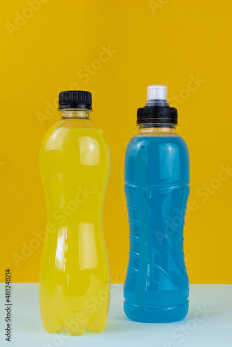 Two bottles of an isotonic drink and L-carnitine, a sports energy drink on a yellow background. Various bottled sports drinks - L-carnitine and isotonic macro. Bottle of fitness drink.