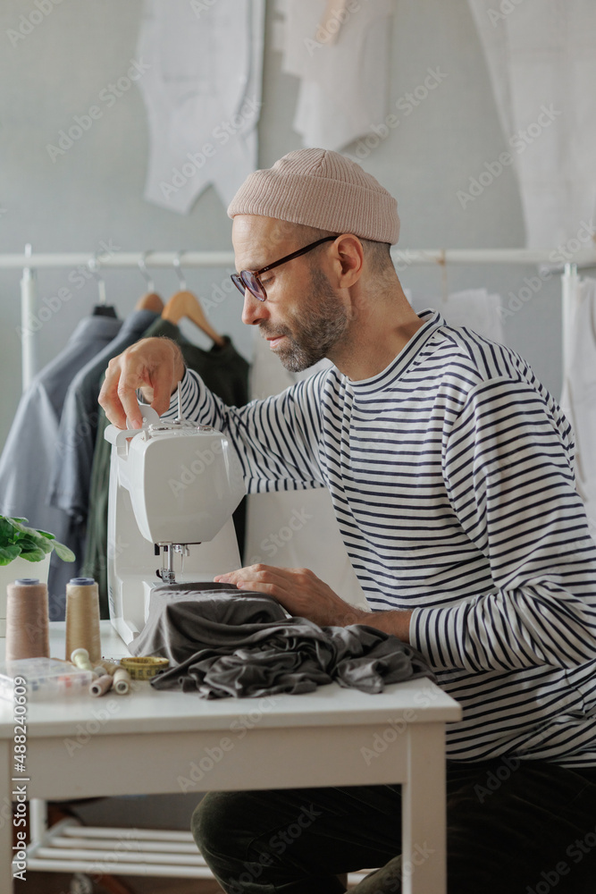 senior male fashion designer or clothing constructor sews on a sewing machine in the workshop and
