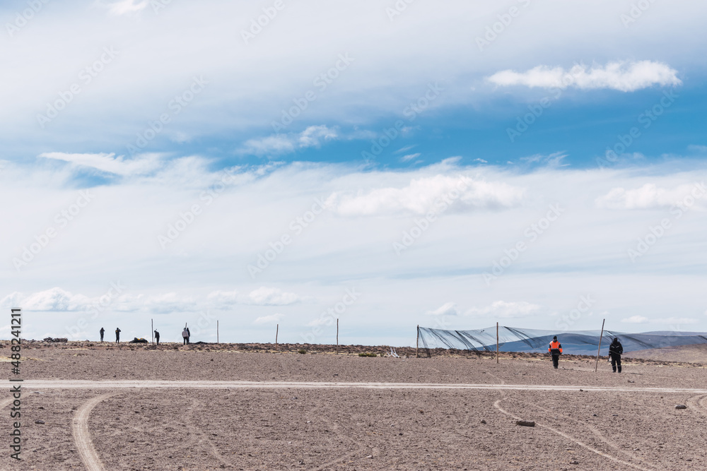 men placing fence for the realization of chaco de vicuñas in the Andes mountain range on a sunny day with clouds and blue sky
