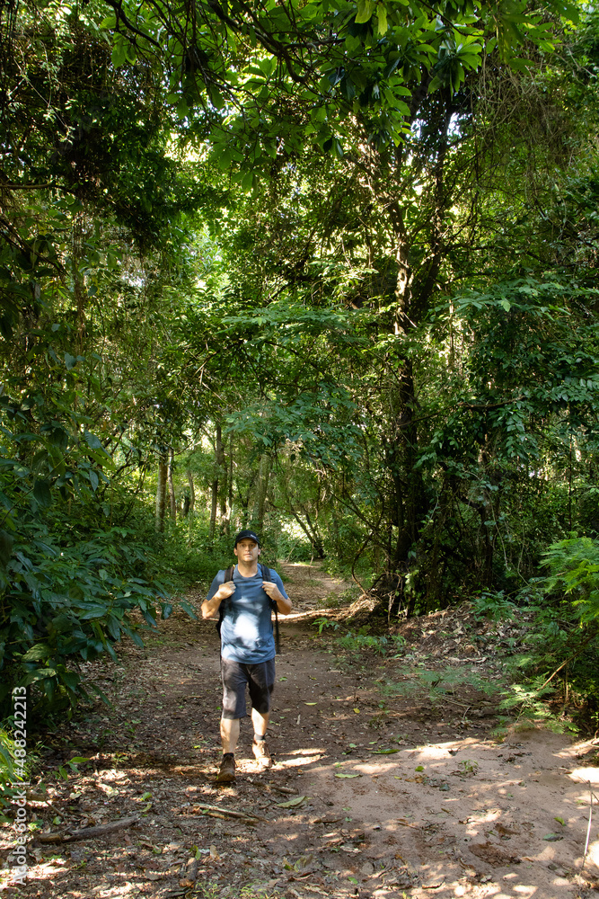 Caucasian man walking in blue t-shirt and black shorts on a trail through the forest with backpack on his back