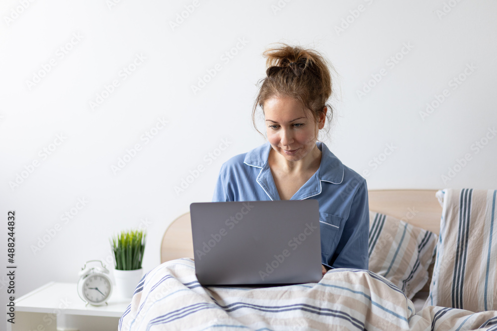 Young woman working in her pyjama from home from her bedroom in the morning. Checking mails, making conference calls, shopping online. Copy space for text Young woman working in her pyjama from home from her bedroom in the morning. Checking mails, making conference calls, shopping online. Copy space for text