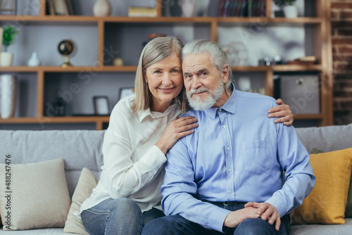 Portrait of senior couple man and woman, family in love, looking at camera and smiling while sitting on sofa at home, and hugging