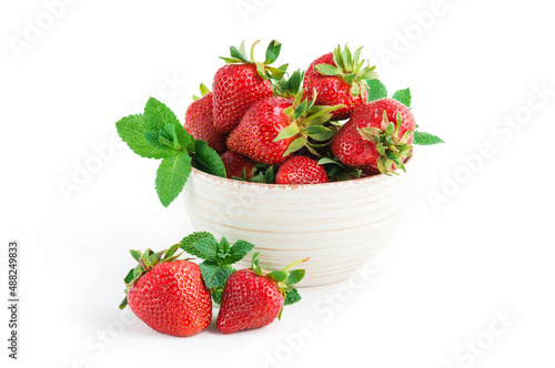 Fresh ripe delicious strawberries in ceramic bowl with leaves of green mint on white background.