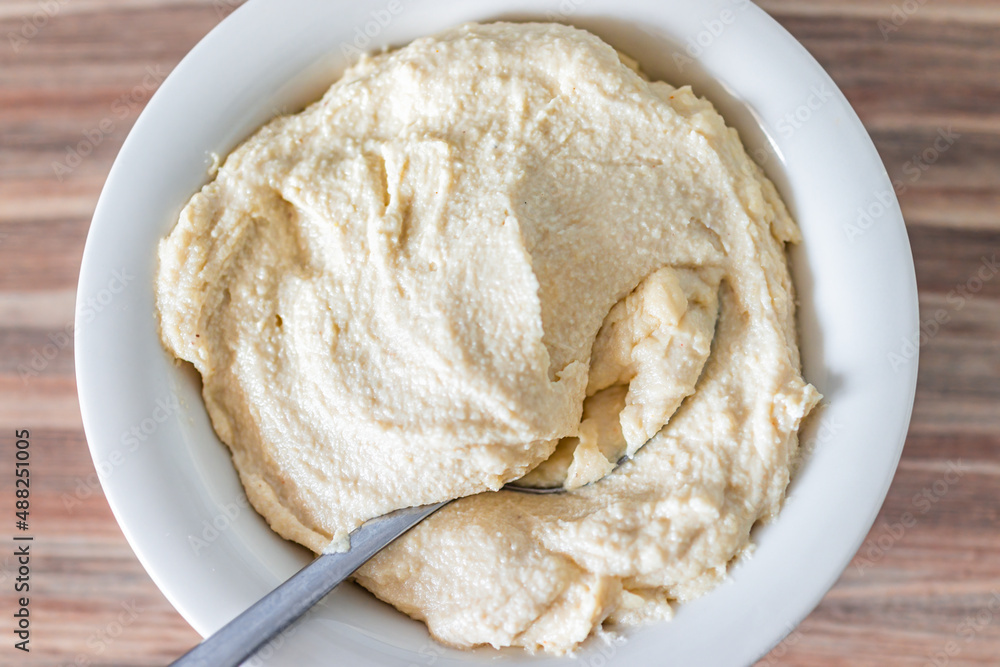 Above flat top view closeup of hummus or vegan cashew cheese spread homemade with nuts, chickpeas spices and garlic in white bowl with spoon Above flat top view closeup of hummus or vegan cashew cheese spread homemade with nuts, chickpeas spices and garlic in white bowl with spoon