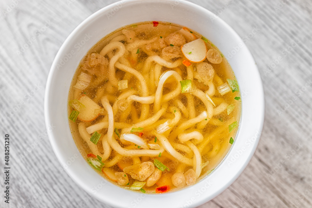 Flat top closeup of Japanese udon ramen noodle instant soup in bowl as asian meal with texture of toppings floating such as fish cakes and green onion Flat top closeup of Japanese udon ramen noodle instant soup in bowl as asian meal with texture of toppings floating such as fish cakes and green onion