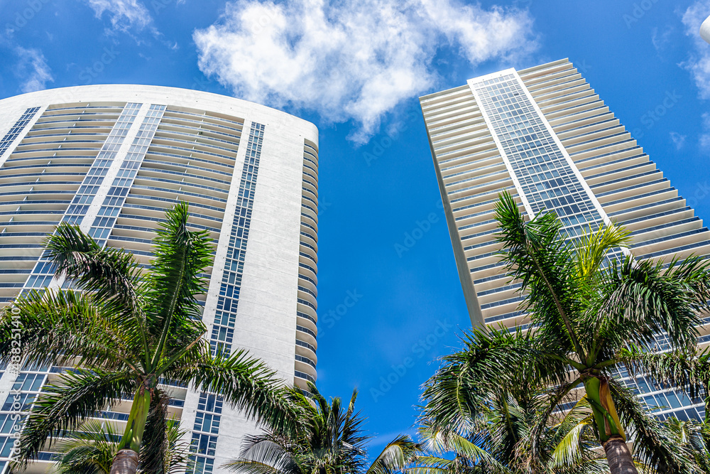 Miami apartment condo buildings in Hallandale Beach, Florida with palm trees on sunny day blue sky looking up low angle view of cityscape