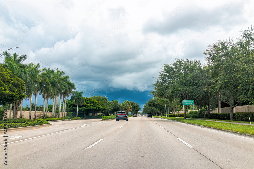 Naples, USA Airport-Pulling open empty road street with cars in traffic on cloudy stormy day with sign driving point of view