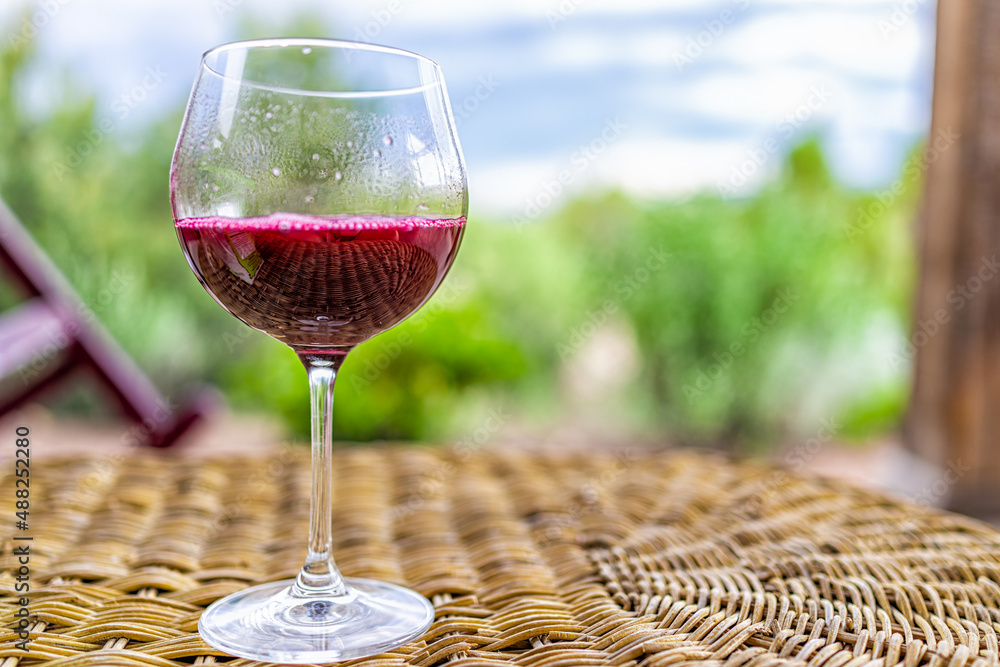 Obraz premium Glass of dark red purple wine or cranberry juice on wicker table in Santa Fe desert garden backyard with closeup of one drink and bokeh background of scenery