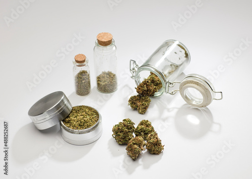 top view of marijuana buds with grinder accessories, glass bottles, and white background