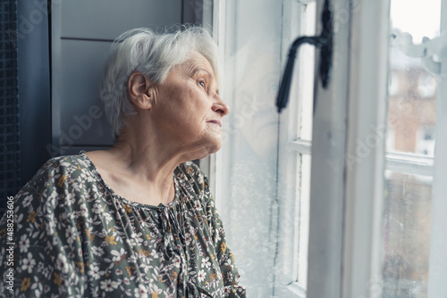 Foto side shot of an elderly European grandmother being all alone during Grandparent's Day and softly gazing out of the window