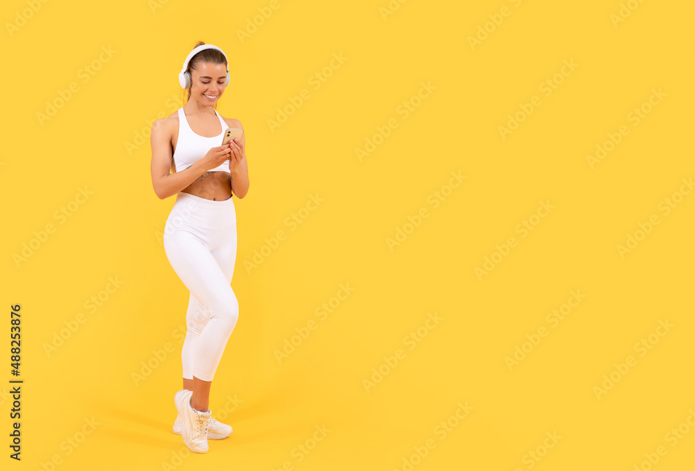 sport woman with headphones and smartphone on yellow background. copy space