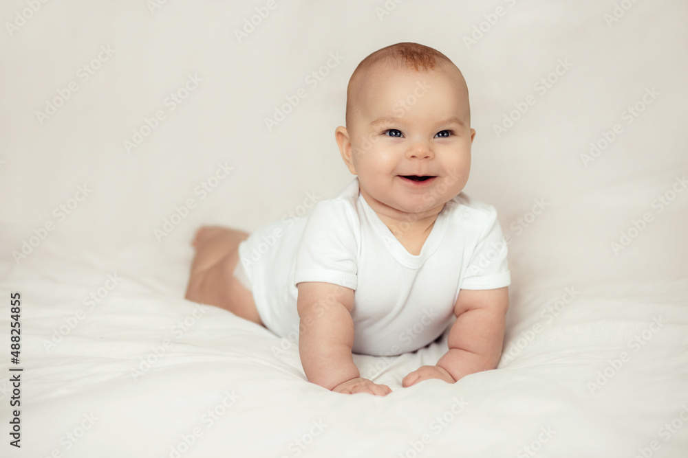 Cute happy baby girl lies on the bed on white sheets.