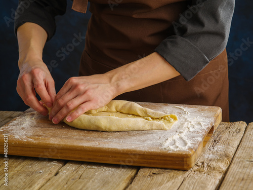 A professional chef prepares pies, dough rolls on a cutting board. Wooden texture, dark background. Close-up. Recipes for restaurant and home cooking. Hotel, restaurant, bakery.