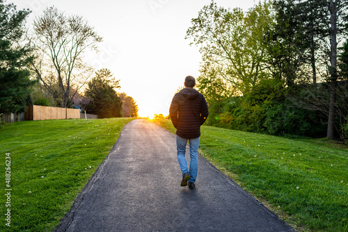 Sugarland Run Stream Valley Trail hike in Herndon, Fairfax county in Virginia spring with paved path road and silhouette of man walking towards sunset as hope concept photo