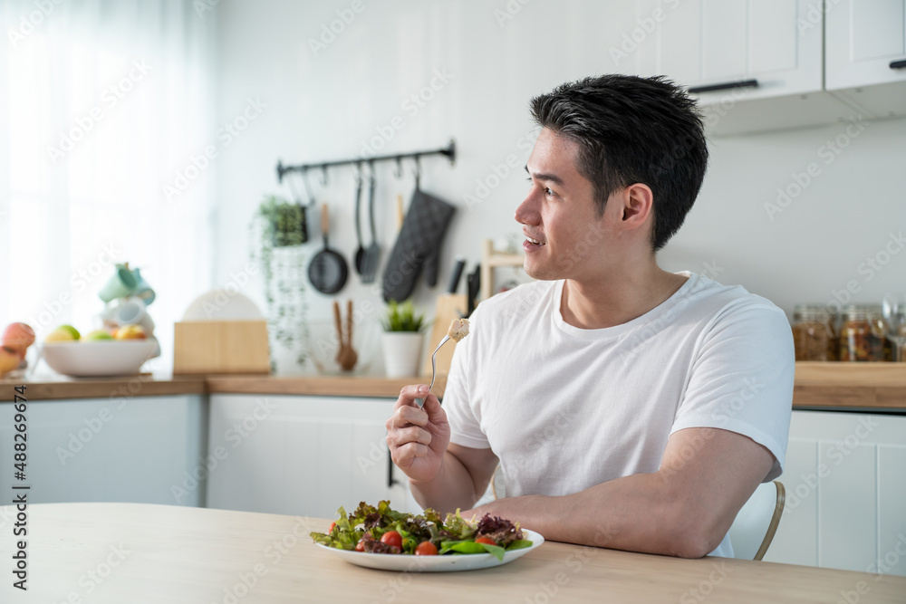 Asian attractive handsome male eating green salad in kitchen at home. Asian attractive handsome male eating green salad in kitchen at home.