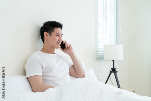 Asian handsome man talk on mobile phone call on bed at home in morning. 