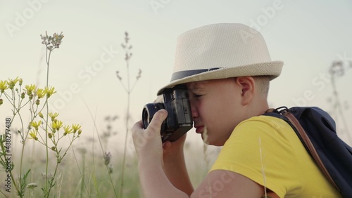 Child boy plays with camera, photographs flowers in summer park. Concept of childrens fantasy in nature. Happy boy, child dreams of becoming photographer. Child dreams of traveling, making discoveries