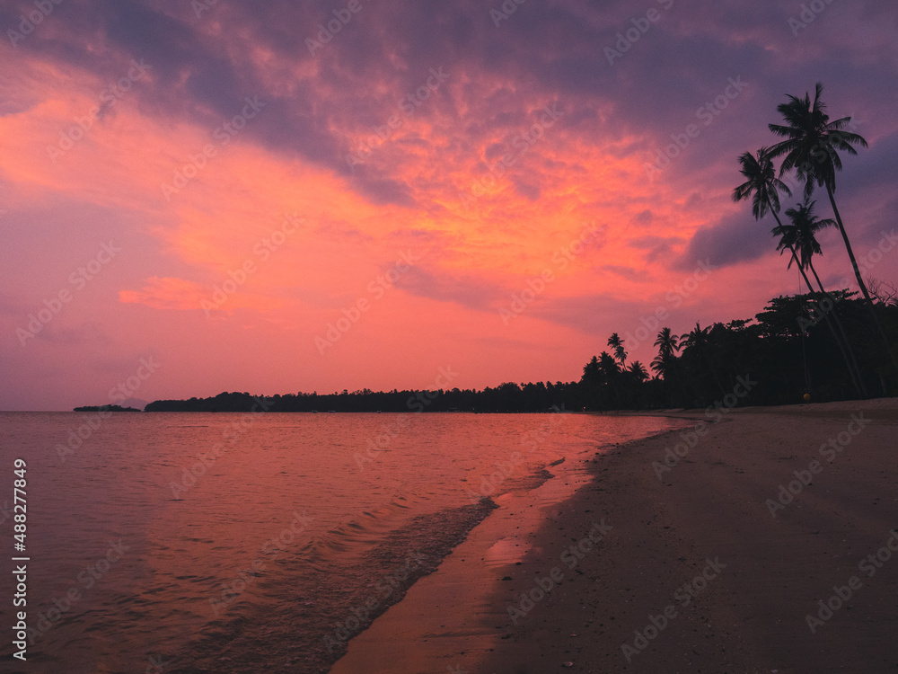 Scenic view of peaceful tropical island beach with iconic tall coconut palm tree against sunset cloudy twilight sky. Koh Mak Island, Trat, Thailand.