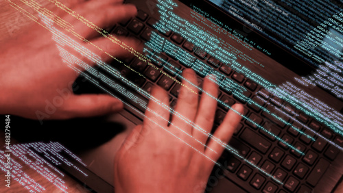 Programmer at work - Caucasian man hands typing on laptop keyboard, elements of software code running on screen and flying in the air. Hacker or coder working with notebook. 