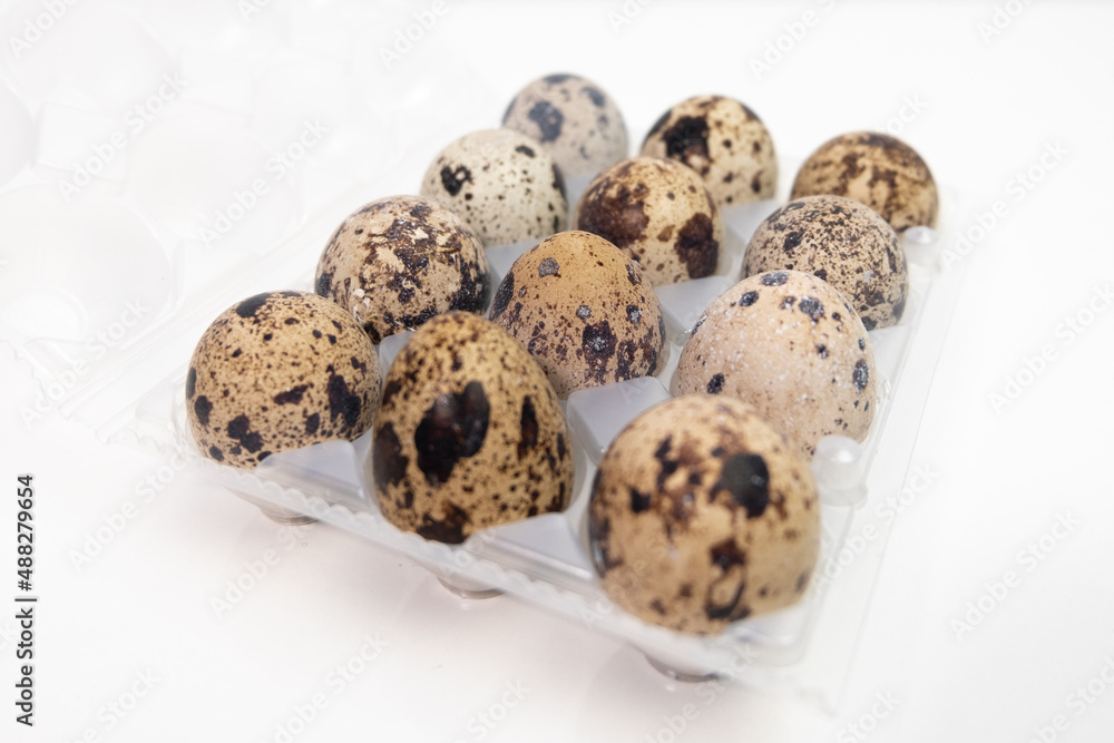 Dozen Quail eggs in a aplastic carton on white.