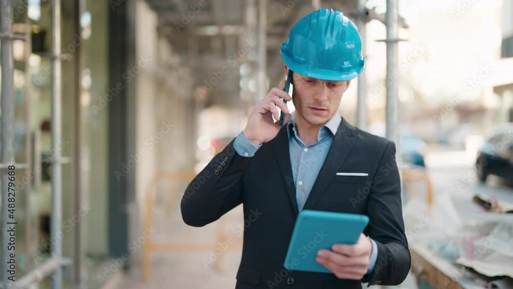 Young caucasian man architect using touchpad and talking on the smartphone at street Young caucasian man architect using touchpad and talking on the smartphone at street