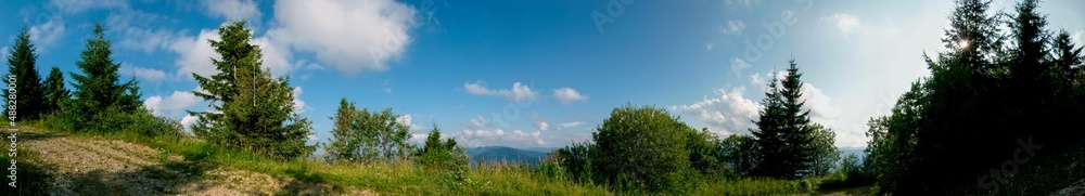 Panorama of a tourist tent on a green meadow on a background of forests and peaks Panorama of a tourist tent on a green meadow on a background of forests and peaks