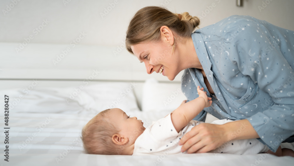 Mother 30 years old playing with her little son on the bed, kid with mom in the morning in the bedroom, child care, the concept of happy motherhood Mother 30 years old playing with her little son on the bed, kid with mom in the morning in the bedroom, child care, the concept of happy motherhood