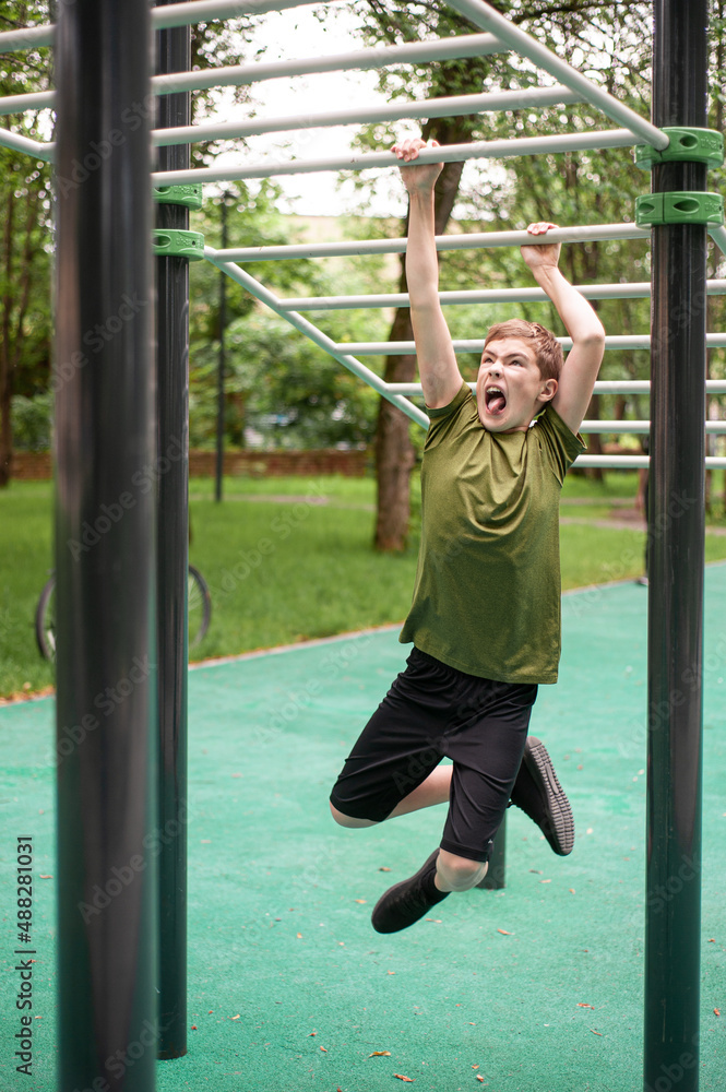 A teenage boy trains in the open air. A young man emotionally moves around the handle with great effort. Body development. Hobbies of teenagers. Vertical photo.