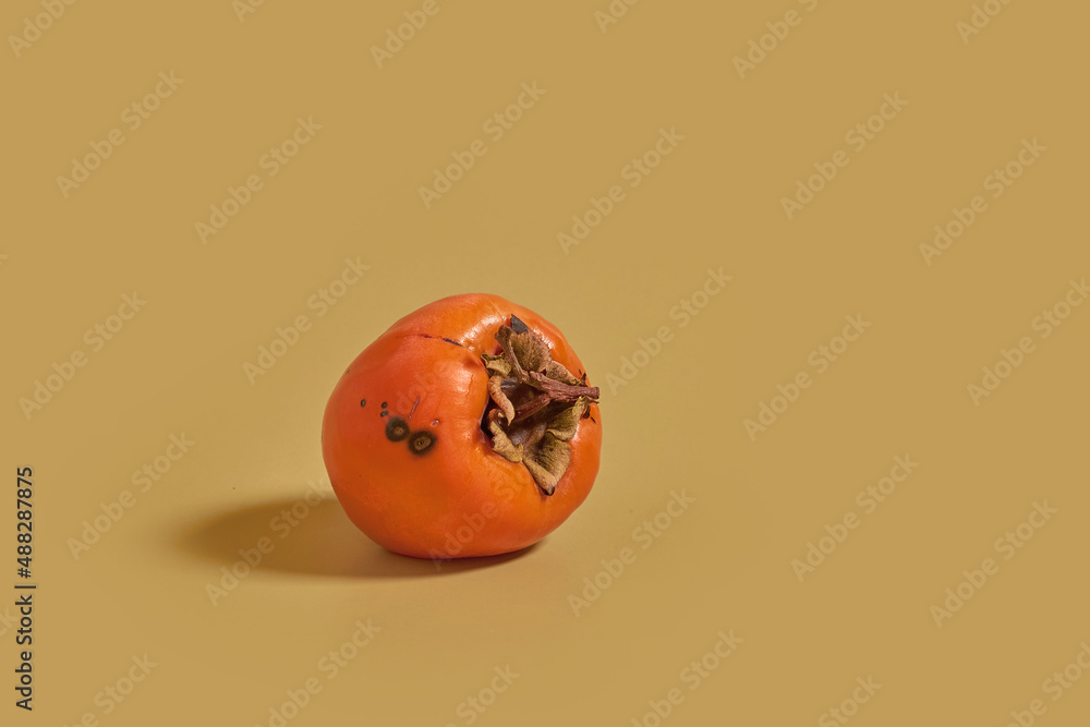 Rotten persimmon on a color monochrome background
