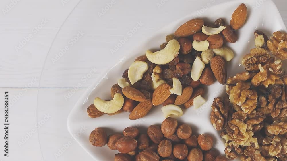 Various nuts close-up on a white plate on a white wooden table. View from above. 4k raw video with smooth camera movement. Various nuts close-up on a white plate on a white wooden table. View from above. 4k raw video with smooth camera movement.