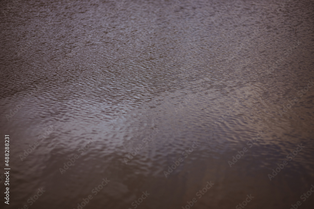 Background, texture from dark waves, in which the sun reflects. Dark waves on the surface of the river in windy weather