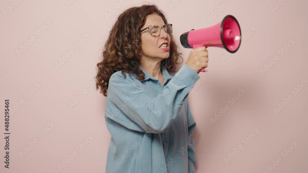 Middle age woman screaming angry using megaphone over pink background Middle age woman screaming angry using megaphone over pink background