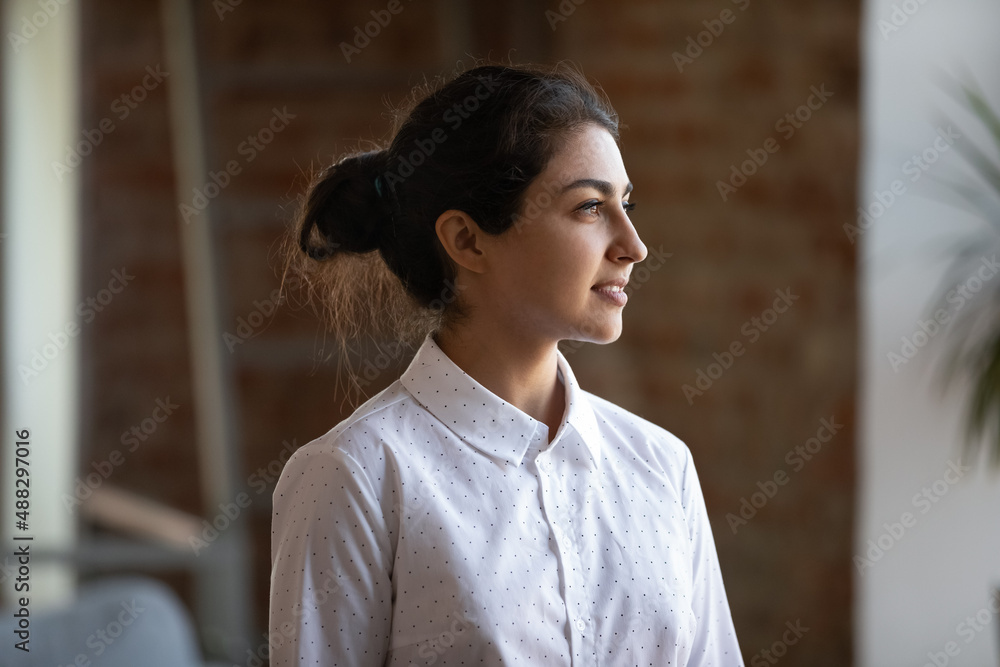 Head shot motivated happy young female Indian business owner employee worker looking in distance, thinking of career opportunities or professional challenges, standing alone in modern workplace. Head shot motivated happy young female Indian business owner employee worker looking in distance, thinking of career opportunities or professional challenges, standing alone in modern workplace.