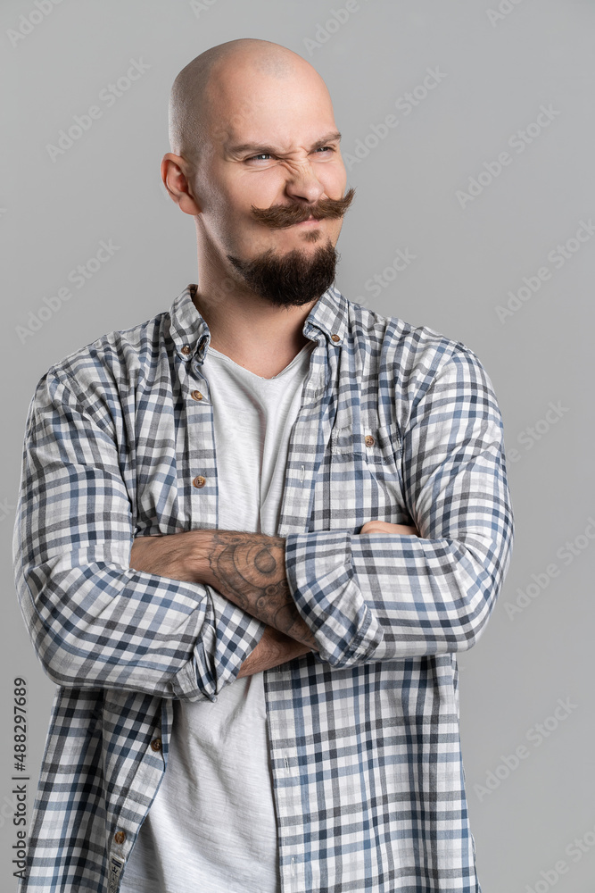 Bald bearded man with mustache isolated on gray background crossed arms looking sceptical aside