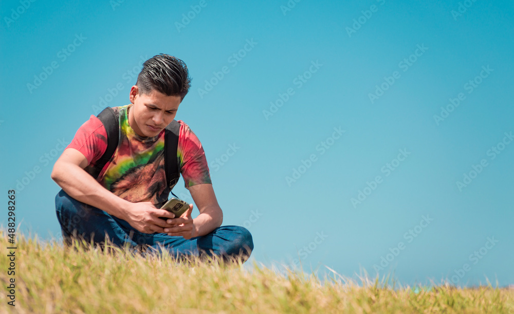backpacker with phone on top of a hill , a man sitting on the grass with his cell phone