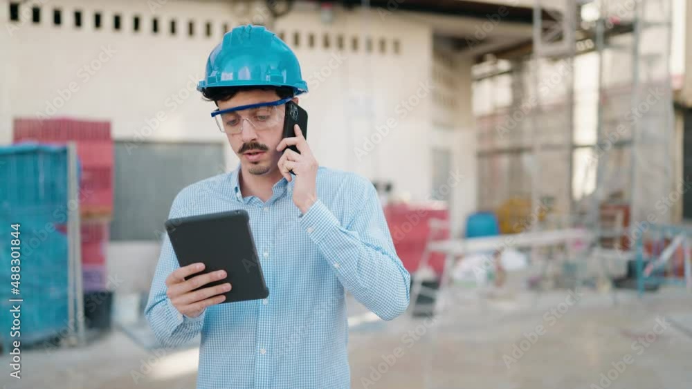 Young hispanic man architect talking on the smartphone using touchpad at street Young hispanic man architect talking on the smartphone using touchpad at street