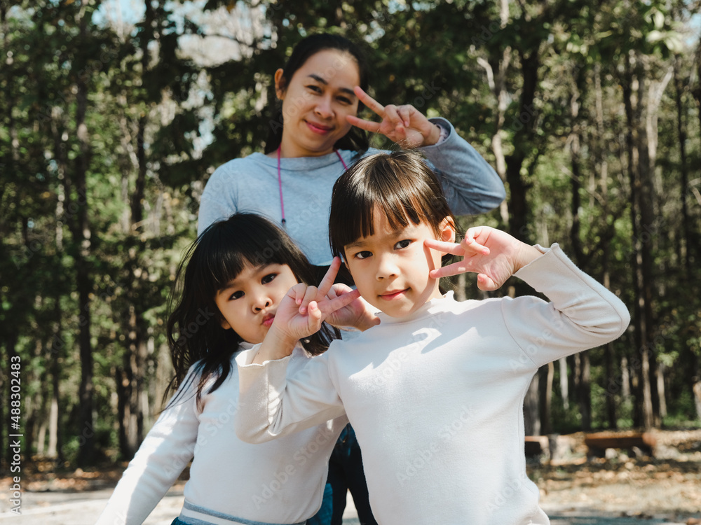 Two cute little Asian girls in summer outfits, having fun with a beautiful young mother smiling happily in the park. Motherhood and family concept. Two cute little Asian girls in summer outfits, having fun with a beautiful young mother smiling happily in the park. Motherhood and family concept.