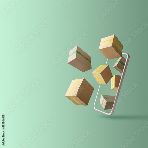 Online delivery concept with copy space. Cardboard boxes on a green background fly out of the smartphone.