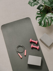 Fototapete Yogaschule Stylish gray and pink home fitness flat lay. Top view of gray sport mat, yoga block, skipping rope and pink dumbbells on neutral carpet background, monstera plant. Set for pilates, fitness, yoga  © fascinadora