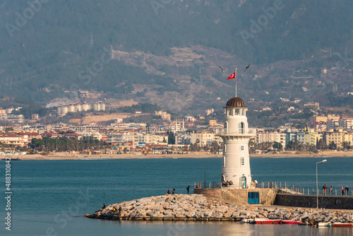 A pier with a beautiful white lighthouse and a pier with many boats and yachts on the background of the blue sea