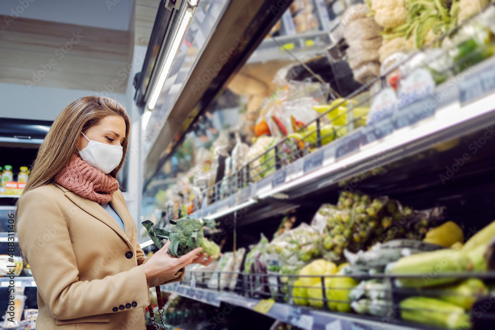 A young woman choosing vegetables during the corona virus pandemic in supermarket.