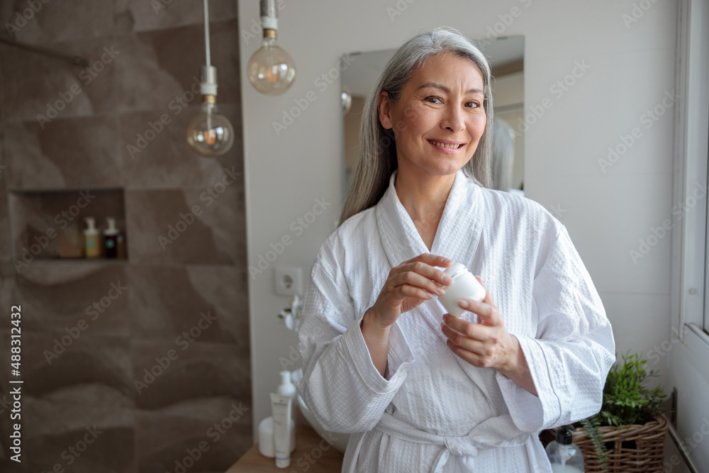 Pretty Asian woman holding cosmetic jar in the bathroom Pretty Asian woman holding cosmetic jar in the bathroom
