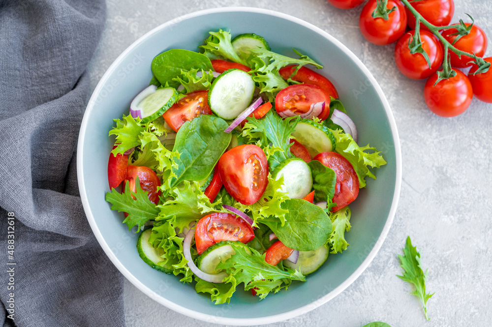 Salad with fresh vegetables and cheese in a bowl on a concrete background. Greek salad, vegetarian dish. Top view.