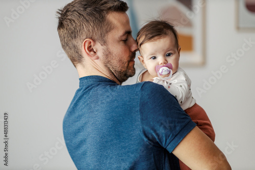 Father holding little daughter with pacifier in the arms.