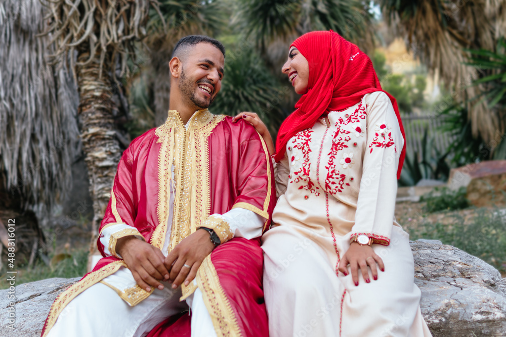 low angle image of a charming arab couple dressed with traditional clothes sitting on a stone and looking each other