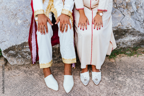 shot of the hands and shoes of an arabian couple dressed with traditional clothes sitting on a stone.