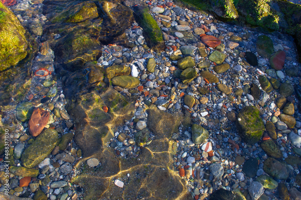 Rocky bottom of a beach with crystal clear waters and stones of different colors
