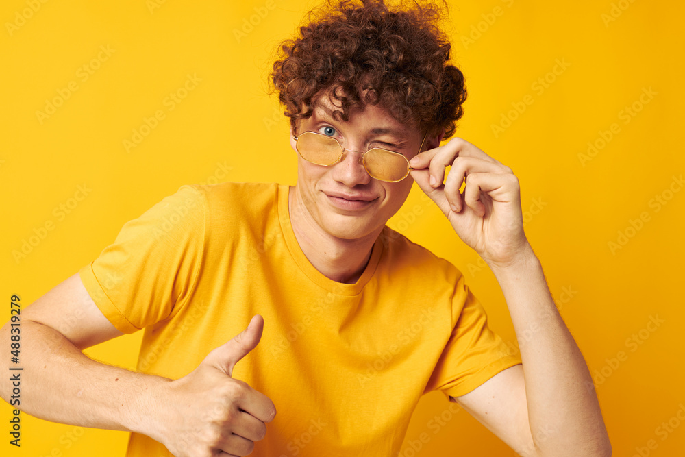 Young curly-haired man wearing stylish glasses yellow t-shirt posing monochrome shot Young curly-haired man wearing stylish glasses yellow t-shirt posing monochrome shot